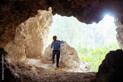 Young man on a jacket and jeans looking up at exiting from a cave