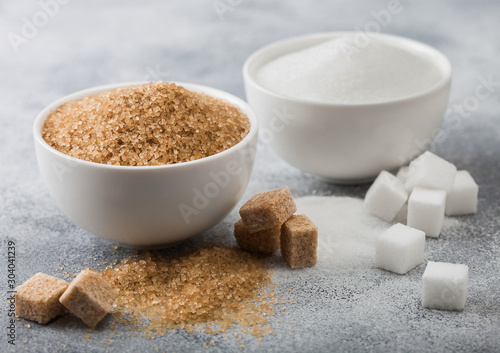 White bowl plates of natural brown and white refined sugar and cubes on light table background. photo