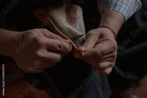 The hands of the shoemaker at work make the sole for new handmade shoes.