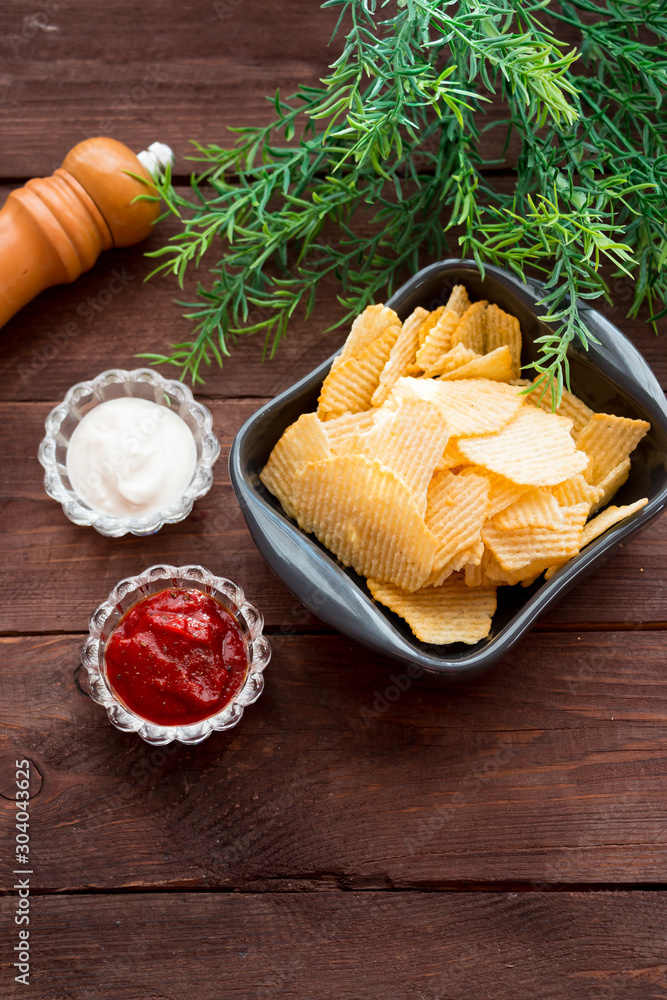 Crispy potato chips in a black ceramic cup, glass plates with sauce, on a dark wooden background. Unhealthy food. Fast foot. Crispy potato chips in a black ceramic cup, glass plates with sauce, on a dark wooden background. Unhealthy food. Fast foot.