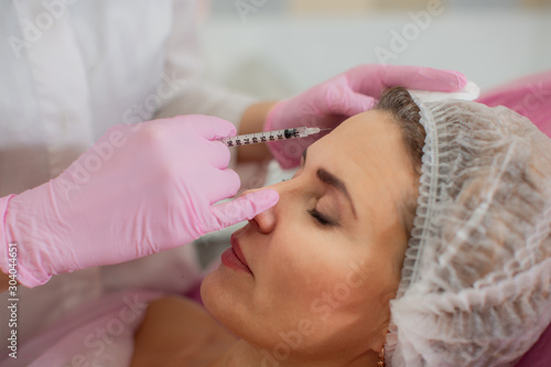 A beautician injects Botox into the facial muscles of his patient's forehead.