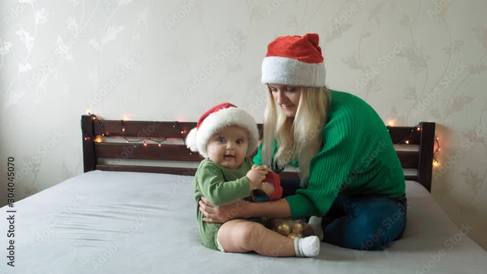 Beautiful woman and her little baby in Christmas caps are playing. New Year theme. Beautiful woman and her little baby in Christmas caps are playing. New Year theme.