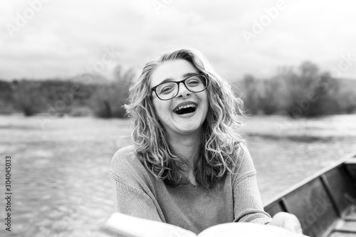 Portrait of young beautiful woman sitting on a boat and reading a book. She is bookworm and she choose between few books. She is holding one book in her hand. 