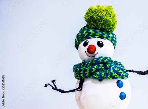 A Christmas snowman dressed in winter warm clothes on a light blue background, offers your products, gifts for New Year's holidays and wishes you a happy Christmas.