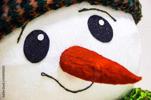 Nice pretty cheerful muzzle of a snowman, with big eyes and a huge carrot in the nose, photographed in close-up.