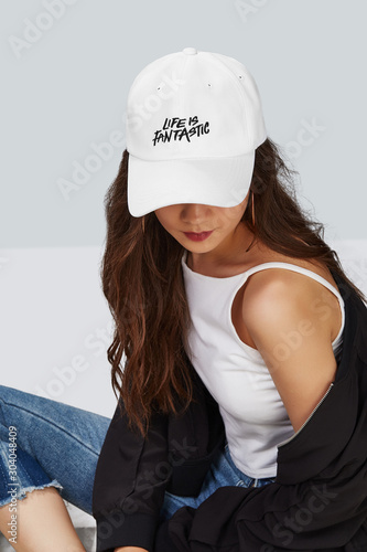 Canvas Print Cropped upward shot of a dark-haired girl, wearing white baseball cap with print with lettering life is fantastic, white tank top and black jacket