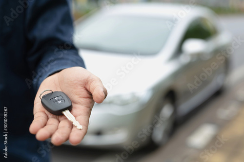 Car key, businessman handing over gives the car key to the other man on car background. 