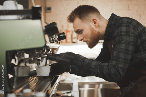   lose up portrait of bearded concentrated barista preparing cappuccino in a coffee shop. Cafe owner is focused on making coffee on a coffee machine  looks like coffee is poured into a cup