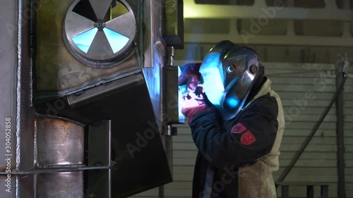 Male welder creates metal body of boiler, large structure, high temperature welding, work in workshop space, smoke and flame, industrial production, skilled worker, blue flashes, sparks fly, workplace