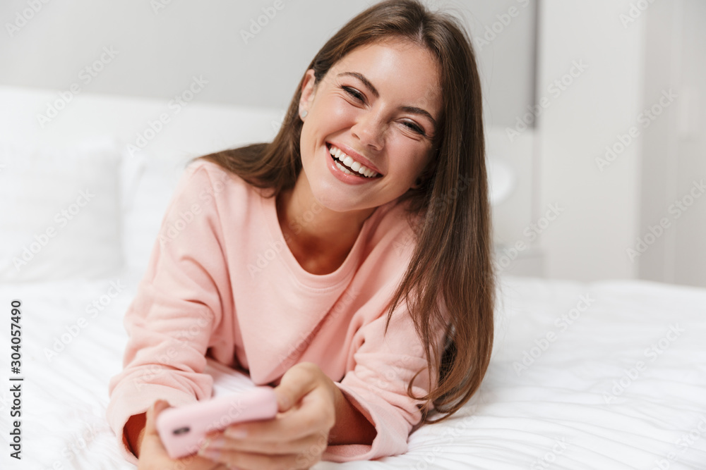 Cheerful lovely young girl wearing pajamas laying in bed