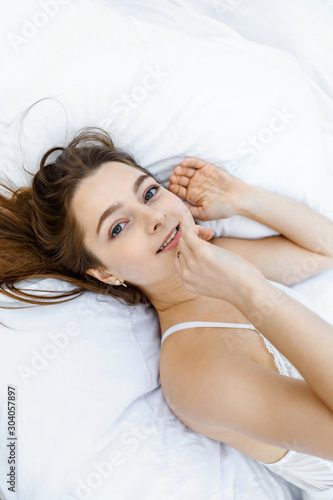 Young slim woman lies on a white bed and smiles
