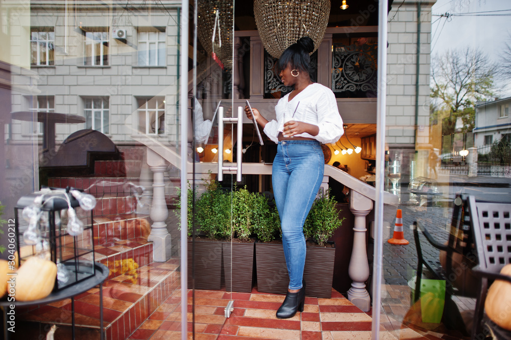 Stylish african american women in white blouse and blue jeans posed at cafe  read menu. Stock Photo | Adobe Stock