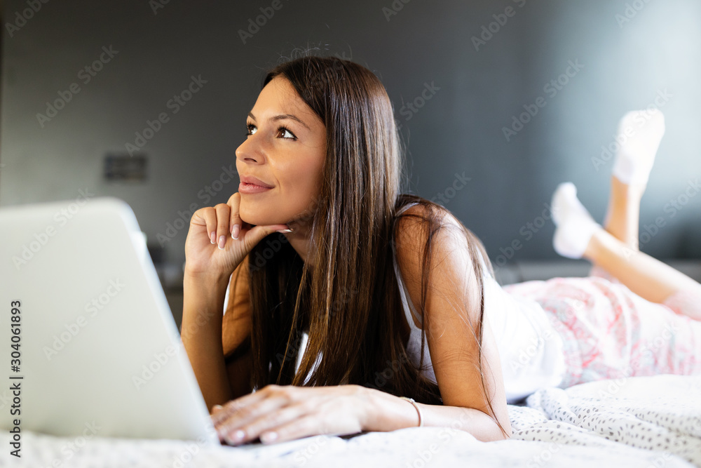 Charming woman lying on bed with crossed legs and laptop in bedroom Charming woman lying on bed with crossed legs and laptop in bedroom