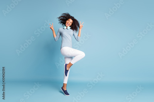 Fototapeta Naklejka Na Ścianę i Meble -  Full length body size photo of cheerful positive nice pretty youngster jumping dancing showing you v-sign in footwear white pants isolated pastel blue color background