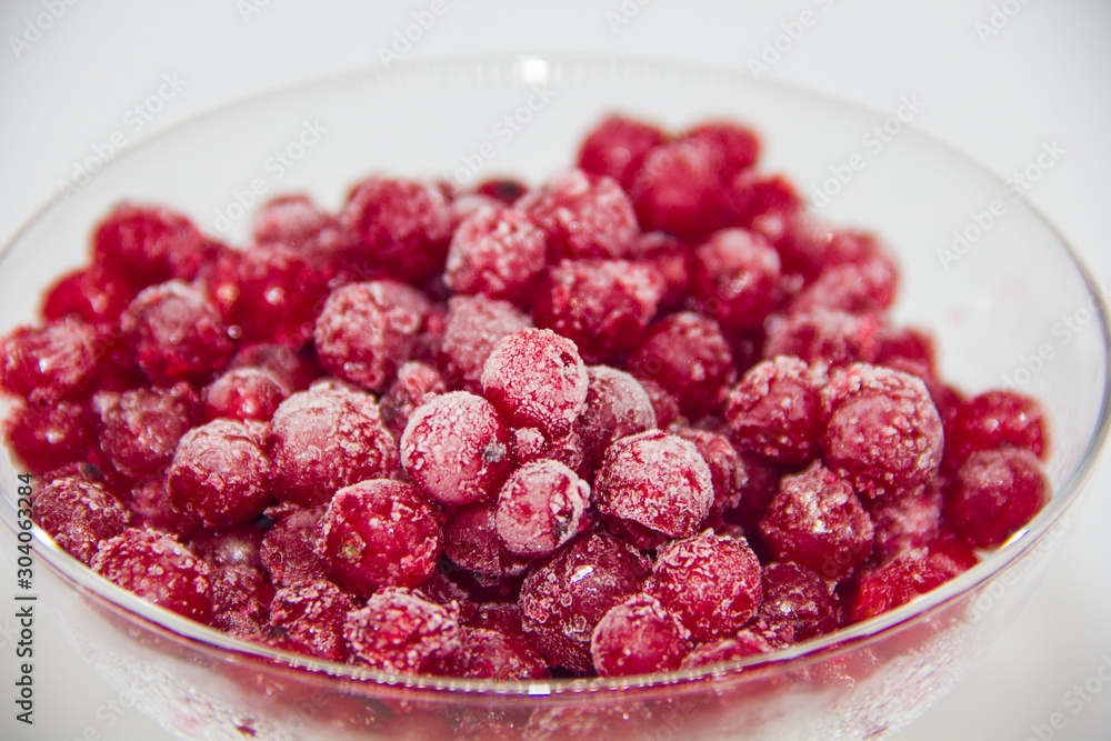 frozen red currants in a glass plate on a white background frozen red currants in a glass plate on a white background