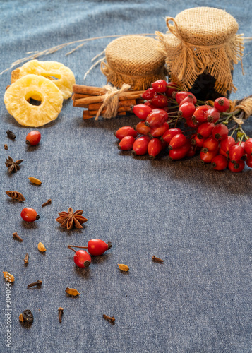 Fototapeta Naklejka Na Ścianę i Meble -  Rosehip berries, buckwheat honey in jars, cinnamon, dried pineapples, star anise on a blue background. Vertical frame, top view, space for copy space.