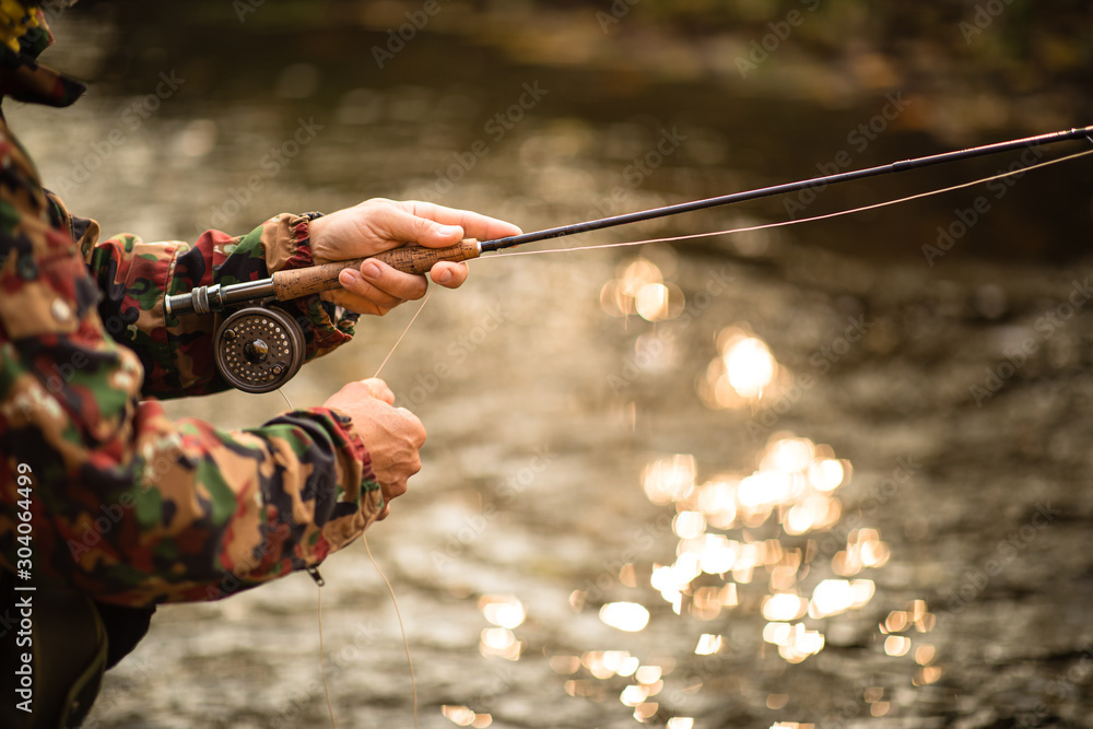 Close-up view of the hands of a fly fisherman working the line and the fishing  rod while fly fishing on a splendid mountain river for rainbow trout Stock  Photo