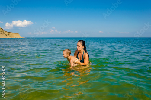 Mom with a young son plays and swims in the sea in the summer.