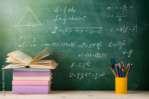 Education and reading concept - group of colorful books on the wooden table in the classroom, blackboard background