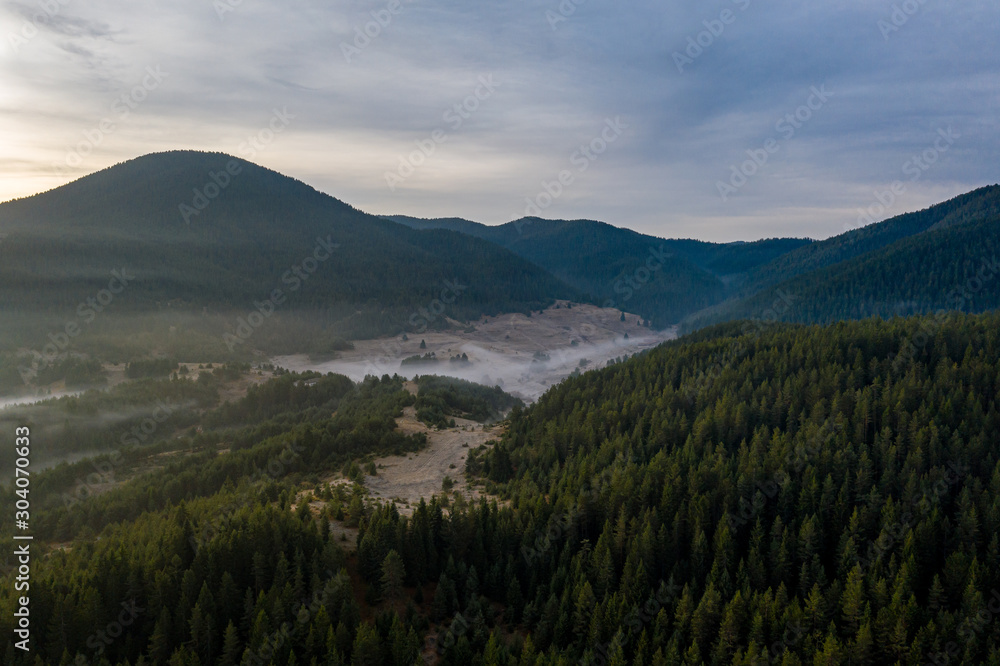 Beautiful sunrise in the mountains with fog crawling between the trees and houses in a village