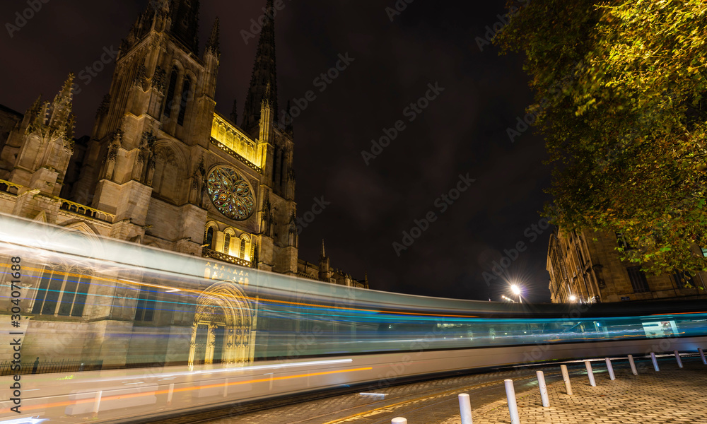 Fototapeta premium Tram passing Bordeaux Cathedral at night in Gironde in New Aquitaine, France