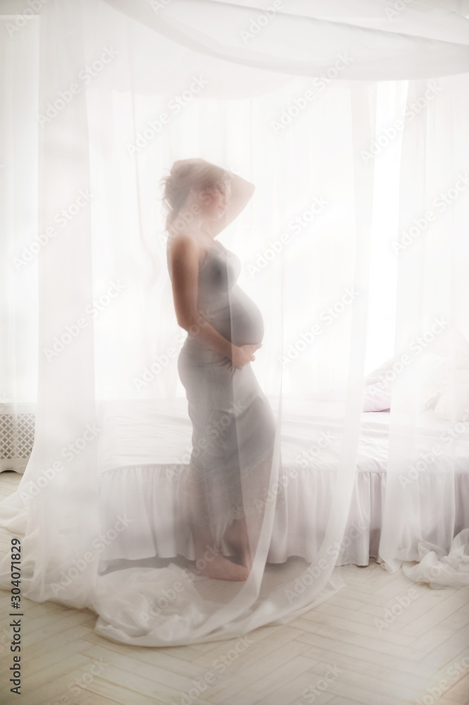 Fototapeta premium Kobieta w ciąży w sypialni z baldachimem biały. W ciąży blisko białego łóżka z bliska i kopia przestrzeń.