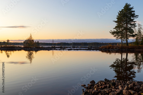 Sunset over a calm lake creating a mirror reflection inside a forest during autumn.