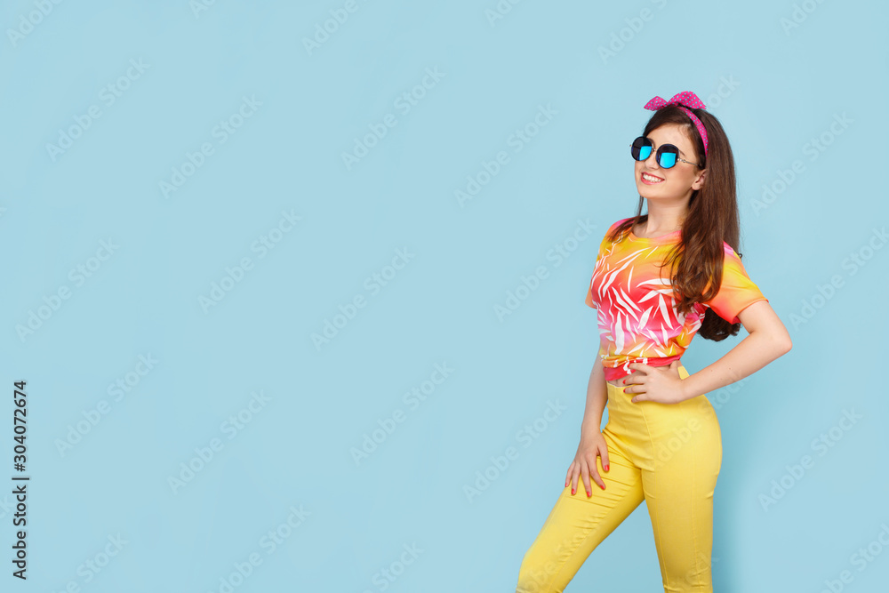 Charming teenager girl, dressed colorful, with sun glasses on a blue background. Horizontal view. Space for text. Charming teenager girl, dressed colorful, with sun glasses on a blue background. Horizontal view. Space for text.