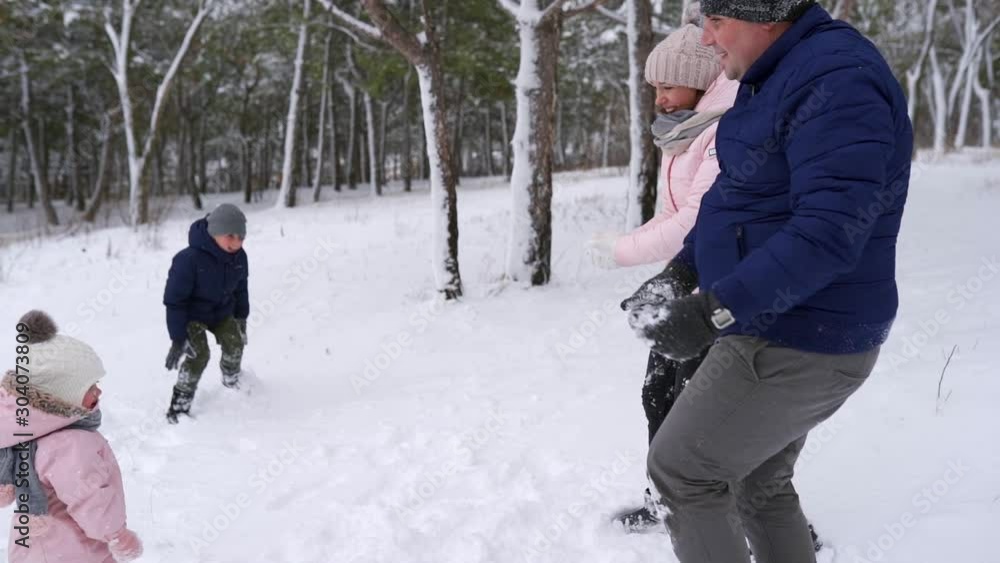 Father, mother, son and little daughter play snowballs in the woods on snowy day. Friendly stylish family have fun with throwing snow in forest. People enjoy winter vacation together. Slow motion. Father, mother, son and little daughter play snowballs in the woods on snowy day. Friendly stylish family have fun with throwing snow in forest. People enjoy winter vacation together. Slow motion.