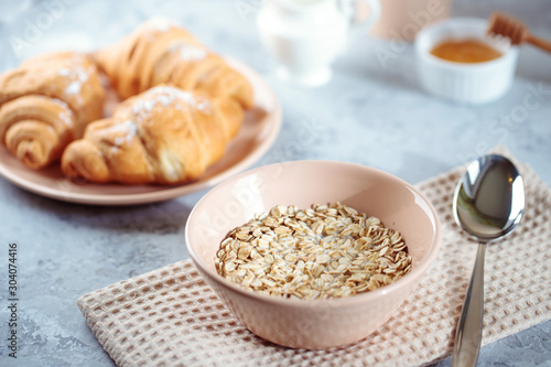 Oatmeal with milk, and croissants with honey on the table. Tasty breakfast.