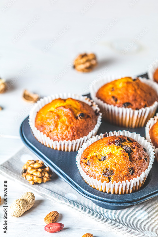 Vanilla caramel muffins in paper cups in bakeware on white wooden background Vanilla caramel muffins in paper cups in bakeware on white wooden background