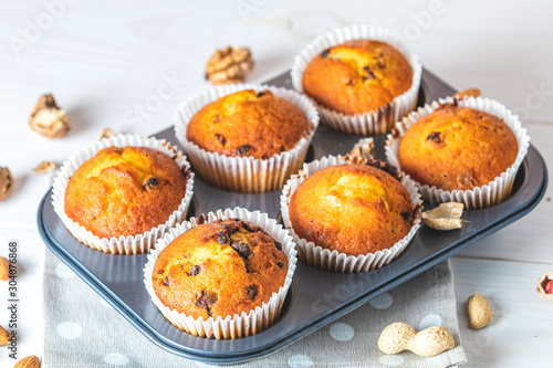 Vanilla caramel muffins in paper cups in bakeware on white wooden background