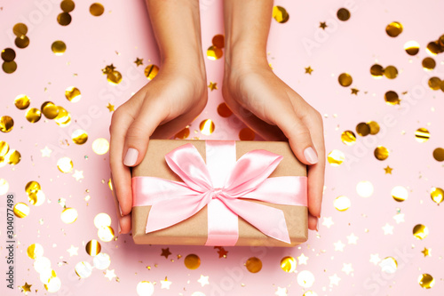 Female hands holding gift present box on festive confetti background.