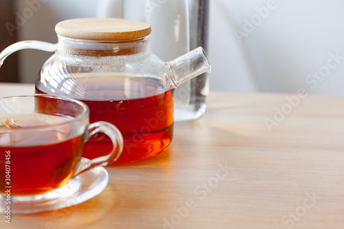 Glass tea pot with black tea on wooden table