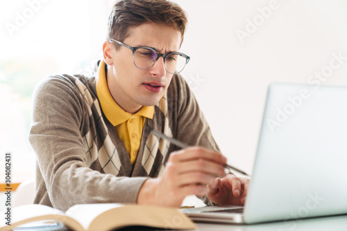 Guy student sit at the table indoors using laptop computer