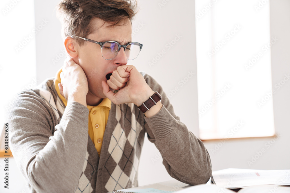 Tired guy student sit at the table indoors yawning. Tired guy student sit at the table indoors yawning.
