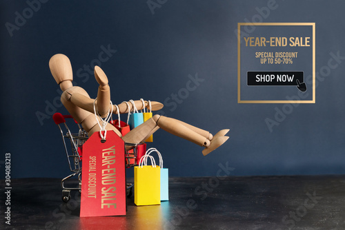 Year-End sale, wooden doll sitting on shopping cart with shopping bag photo
