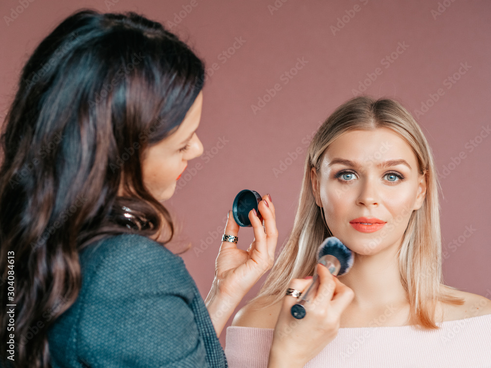The professional makeup artist at work. Applying makeup on a model. Pastel tones. Blond hair and red lipstick The professional makeup artist at work. Applying makeup on a model. Pastel tones. Blond hair and red lipstick