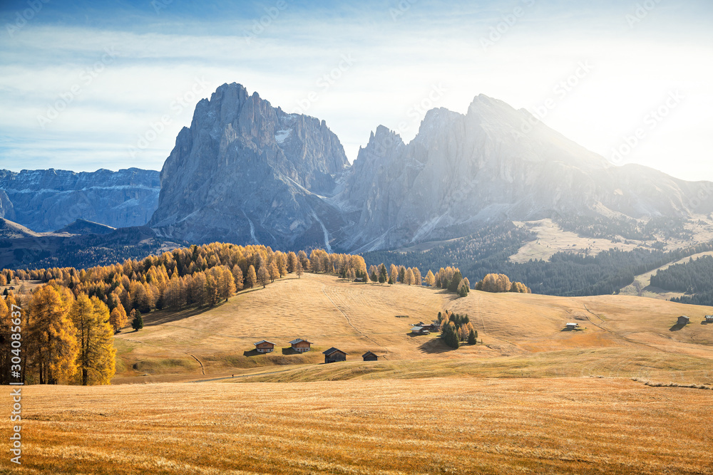 Beautiful view of scenic alpine landscape with traditional wooden chalets on scenic Alpe di Siusi with famous Langkofel mountain peaks in bright morning light at sunrise, Dolomites, South Tyrol, Italy