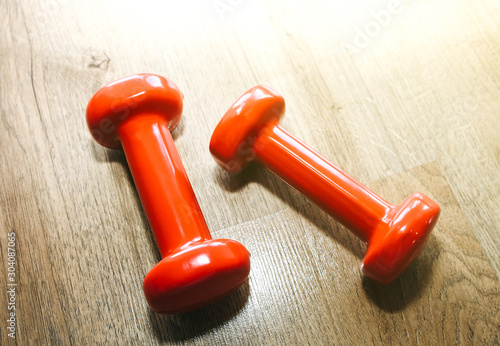 Small red dumbbells on the wooden floor. Fitness gears in the gym. Sport and healthy lifestyle concept.