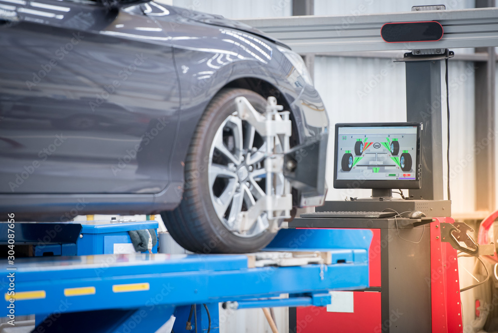 Car mechanic installing sensor during suspension adjustment. Wheel alignment work at repair service station - obrazy, fototapety, plakaty 