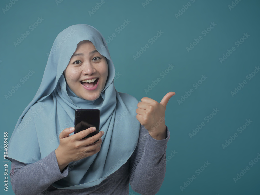 Muslim Woman Holding Phone and Pointing Side, Presenting Something Muslim Woman Holding Phone and Pointing Side, Presenting Something