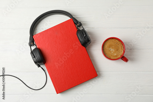 Red book, headphones and coffee cup on wooden background, space for text