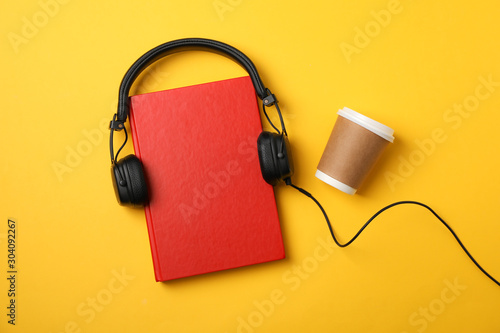 Red book, headphones and coffee cup on yellow background, space for text