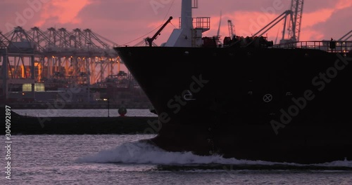 Cargo ship entering the Port of Rotterdam in the darkness of the evening. Bulbous bow in front,