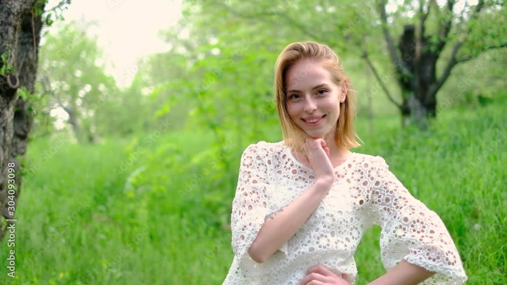 Beautiful attractive young woman posing in spring park wearing white knitted top and blue jeans,, slow motion Beautiful attractive young woman posing in spring park wearing white knitted top and blue jeans,, slow motion