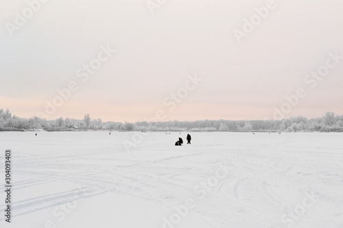 Natural winter landscape in frost, winter at dawn. Silhouettes of fishermen on a snowy river in the distance.