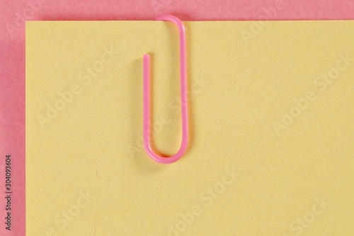 Close-up of a paper clip holding a yellow paper sheet. pink paper clip on yellow sheet of paper  macro shot 
