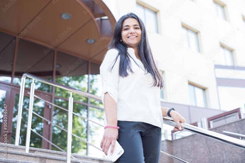Portrait of a beautiful young indian girl. Business woman in office building smiling in hand holding smartphone