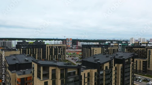 Modern residential area with playground, cars parked along street. Flying of drone above apartment blocks in suburb. Sleeping area in ecologically clean area near forest away noisy city.